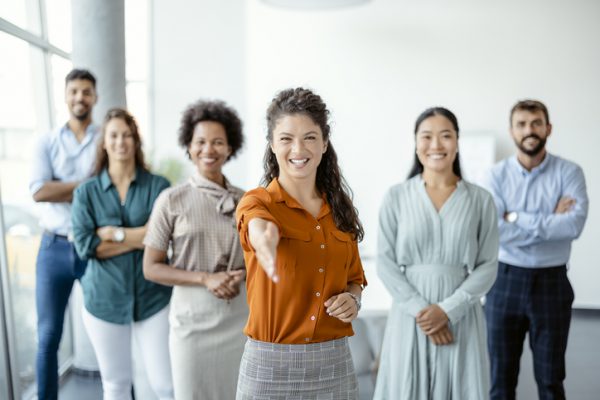 Head shot portrait smiling businesswoman offering handshake, standing with extended hand in modern office, friendly hr manager or team leader greeting or welcoming new worker.