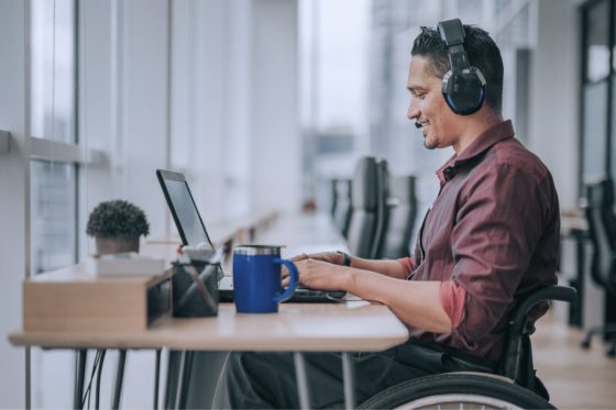 Man in a wheelchair working on a laptop with headphones on