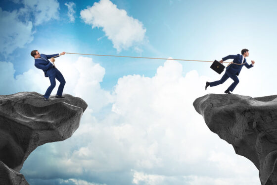 Man holding onto another man across a rock gap with a rope