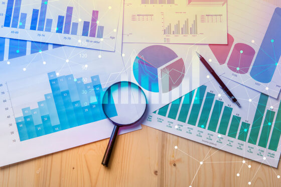 Multiple sheets with data on them spread across a table with a magnifying glass