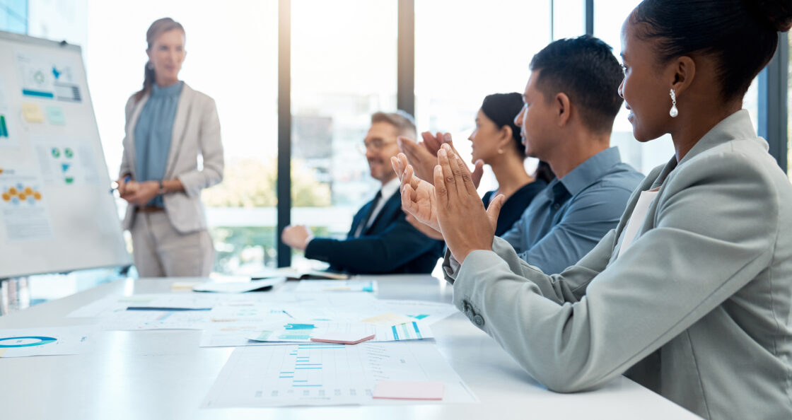 Team of sales reps around table applauding coaching presentation