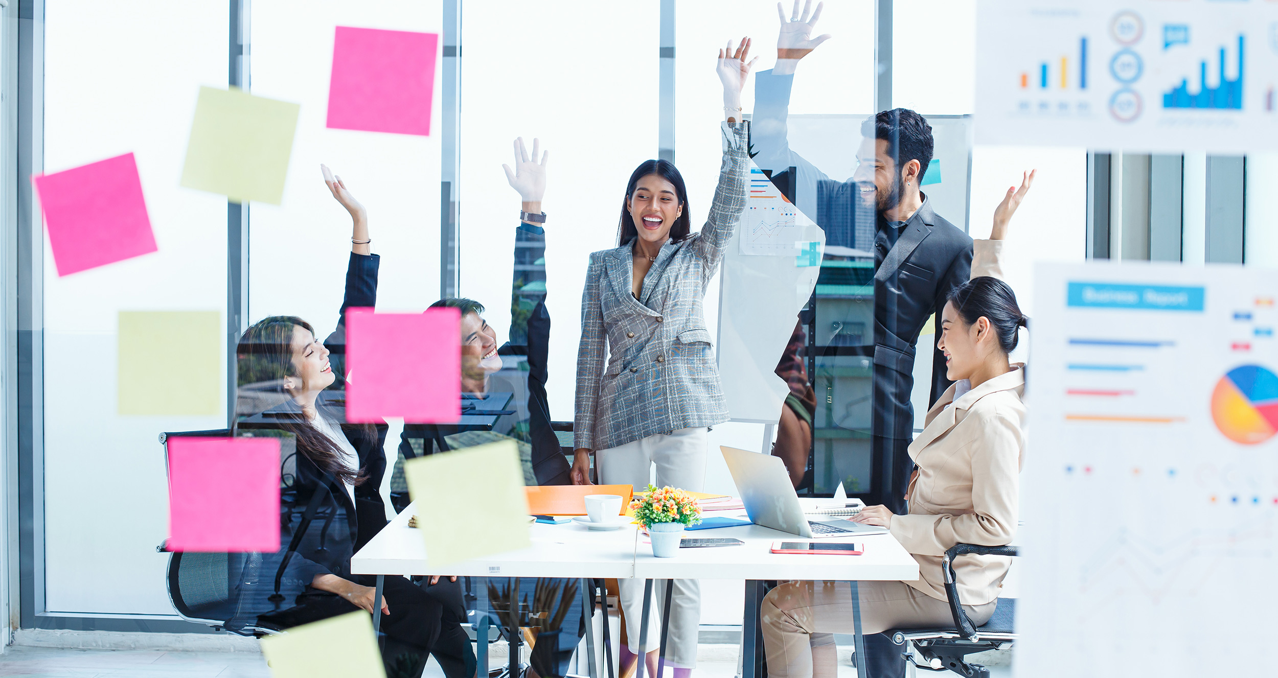 Team of sales leaders sitting in conference room raising their hands