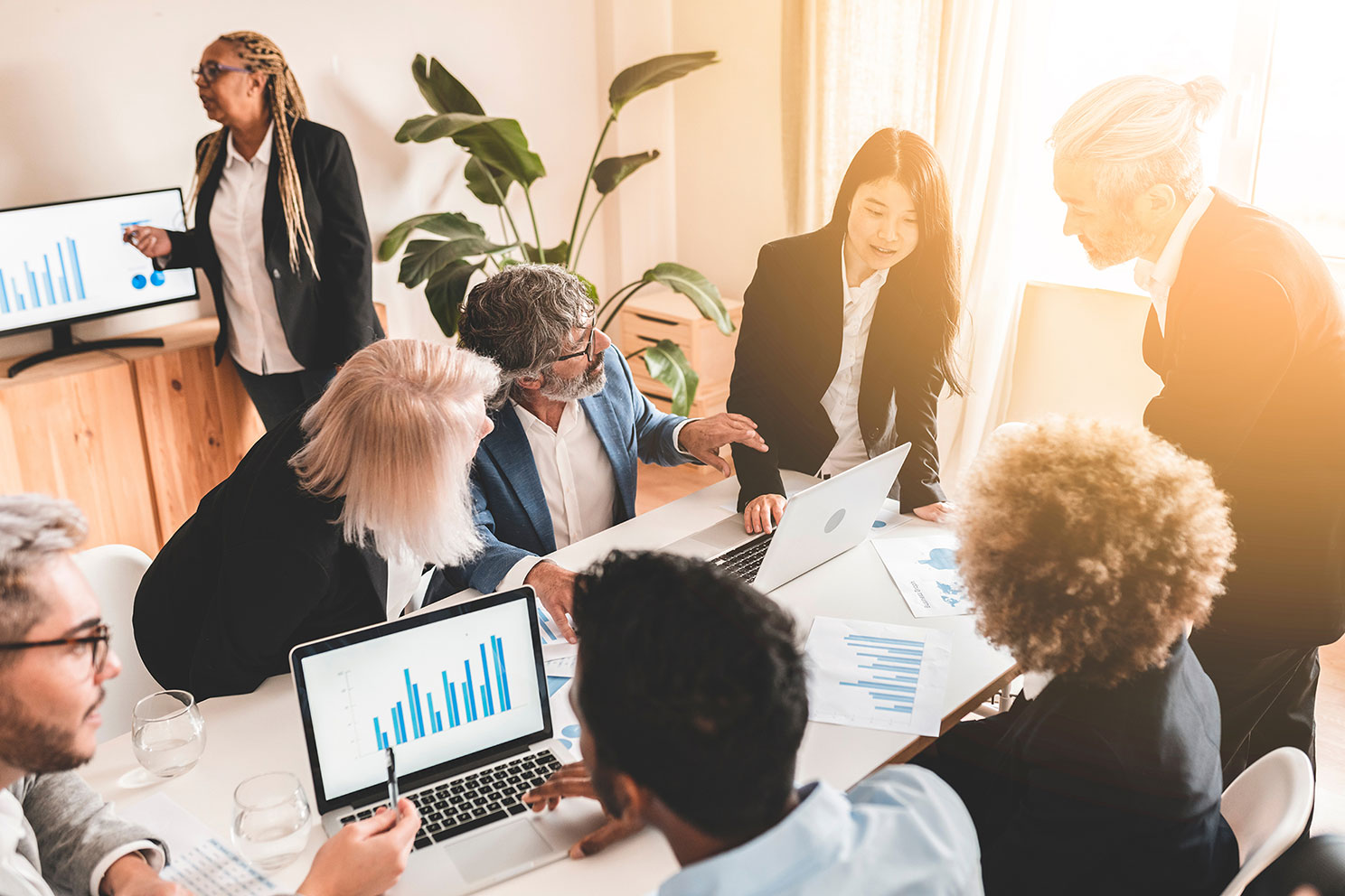 Team of sales reps in conference room reviewing data spread out on table 