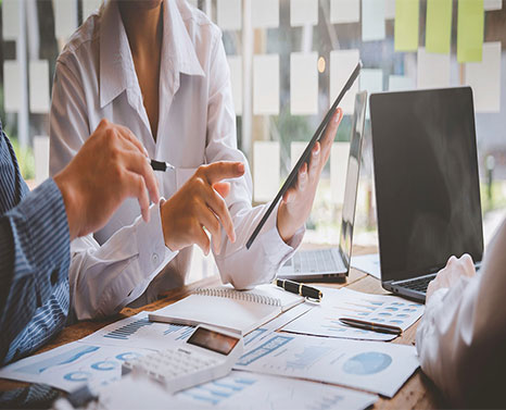 Sales reps gathered around a table reviewing data on tablets, computers, and paper