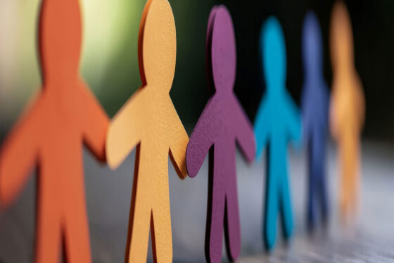 Colorful paper cutout figures holding hands in a row, symbolizing diversity, unity, and teamwork. 