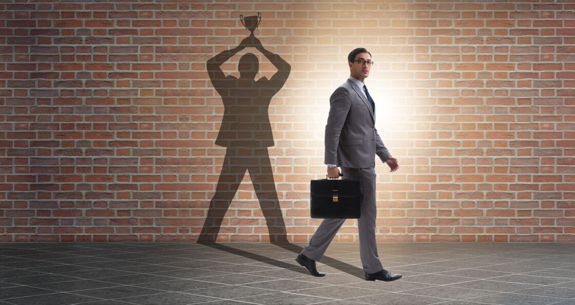 sales leader walking with brief case while his shadow shows him holding a trophy above his head